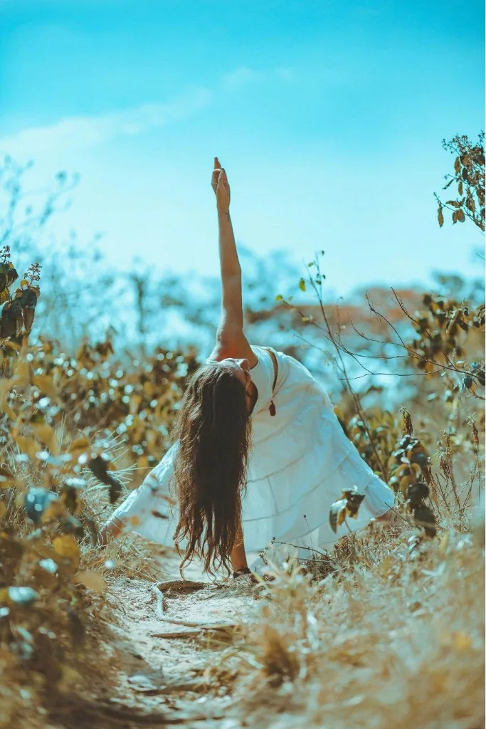 Liis Ugandi в боковом наклоне в сухой траве, белое платье, синее небо. Goyoga Tallinn.